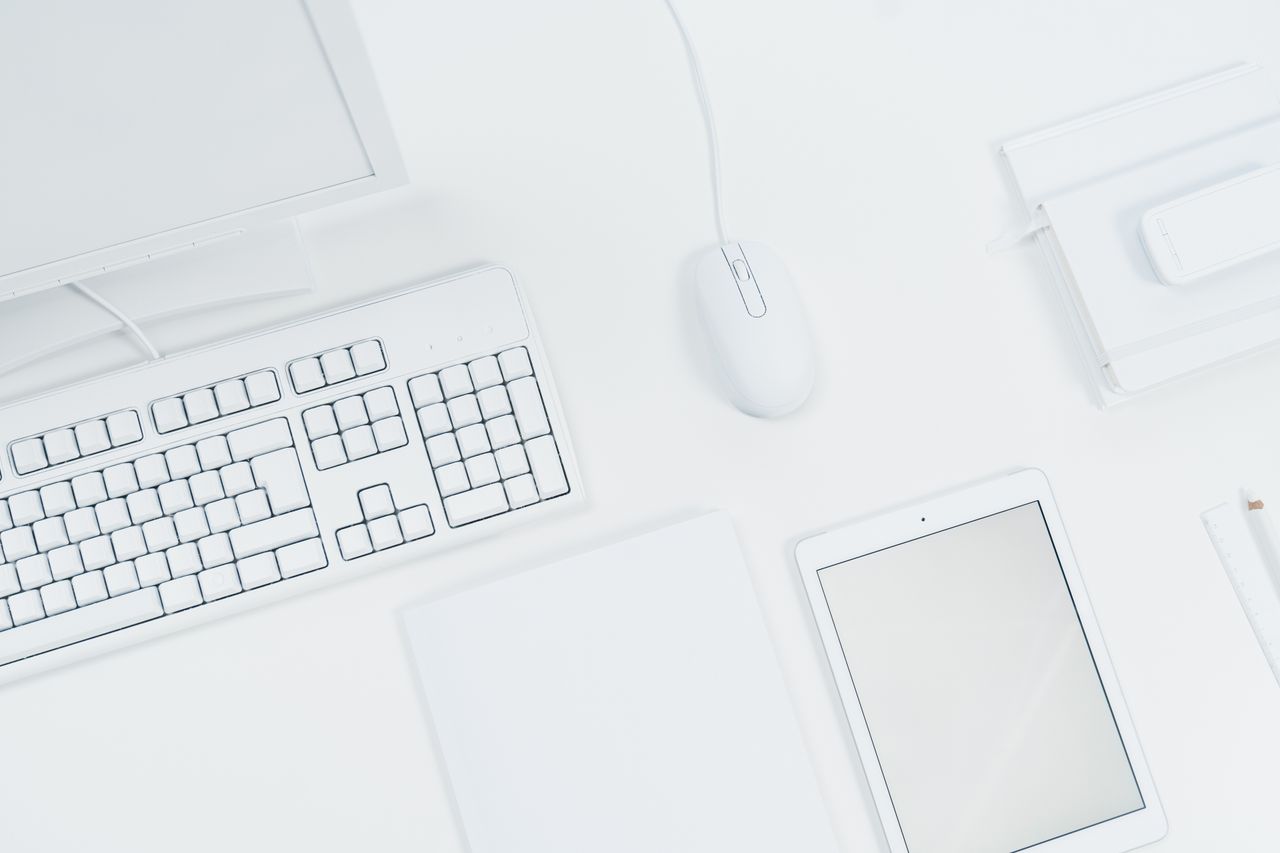 A clean, minimalist workspace featuring a keyboard, mouse, and tablet on a white desk.